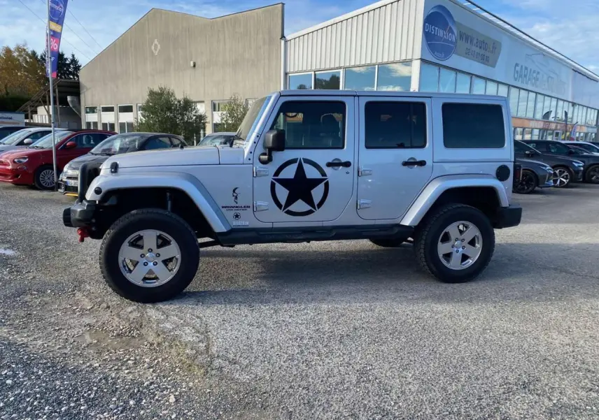 Profil côté gauche d'un Jeep Wrangler gris clair 2012 avec étoile noire militaire sur la porte, stationné en extérieur.