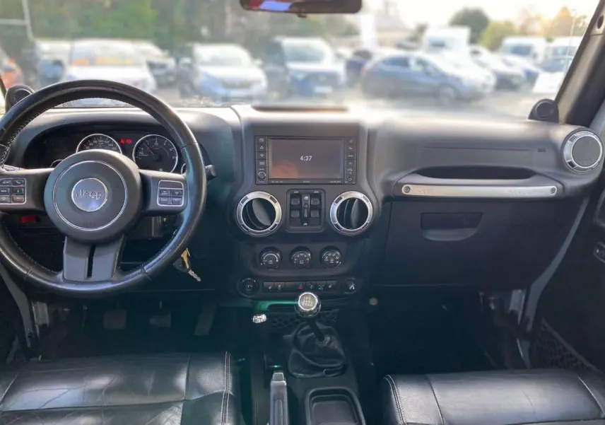 Intérieur du Jeep Wrangler 2012 gris clair, vue frontale sur le tableau de bord avec volant, écran et levier de vitesses manuel.