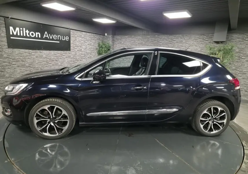 Profil côté gauche d'une DS4 violet foncé métallisé avec jantes alliage et poignées chromées en intérieur showroom.