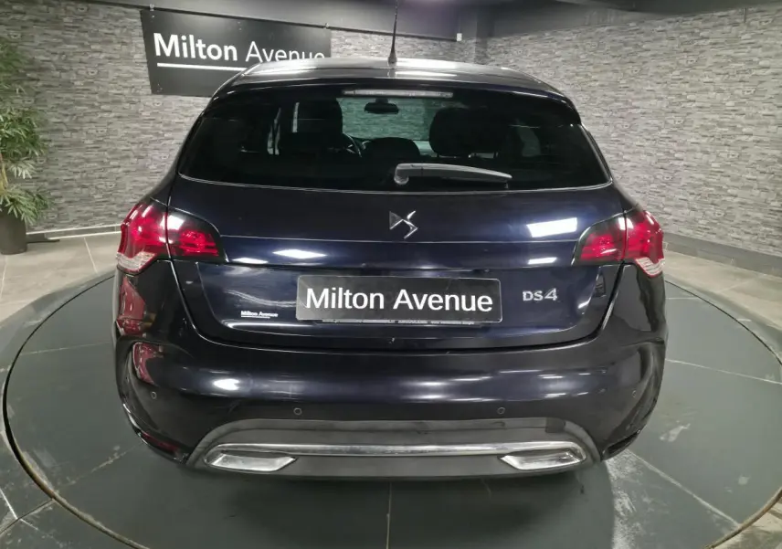 Vue arrière d'une DS4 violet foncé avec feux rouges et double sortie d'échappement chromée dans un showroom.