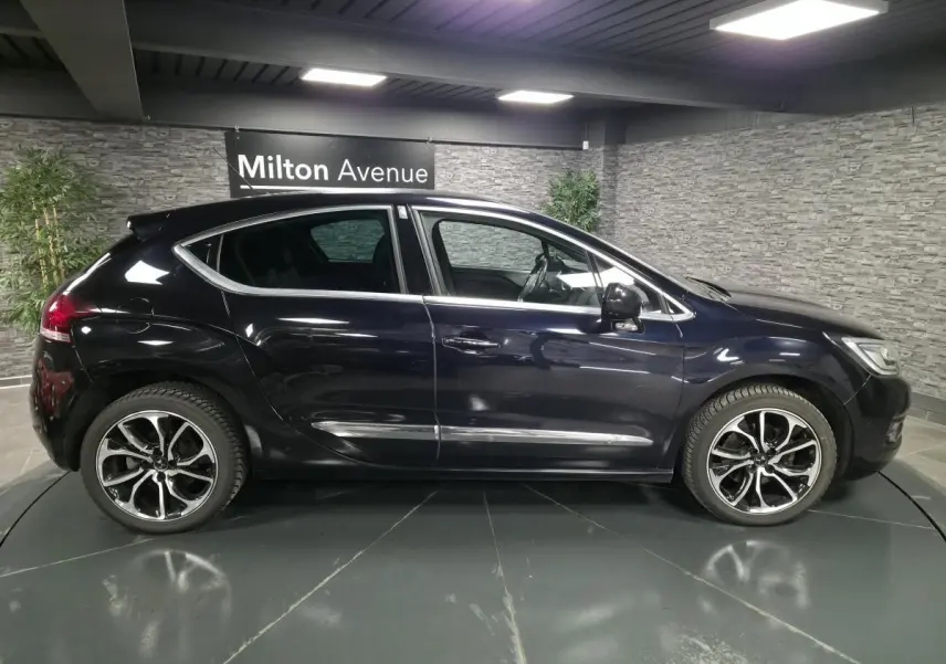 Profil droit d'une DS4 violet métallisé avec jantes alliage noires et baguettes chromées dans un showroom intérieur.