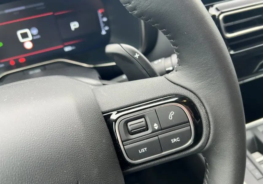 Gros plan sur le volant cuir noir du Citroën C5 Aircross Hybrid 145, avec commandes audio et palettes au volant visibles.