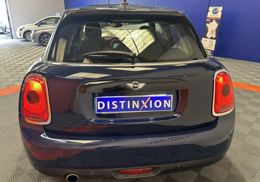 Vue arrière d'une MINI 5 portes Cooper D bleu foncé avec feux rouges et toit ouvrant visible en intérieur showroom.
