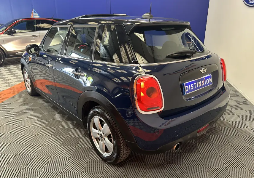 Vue 3/4 arrière droite d'une MINI 5 portes Cooper D bleu foncé avec toit ouvrant, en intérieur sur sol damier.