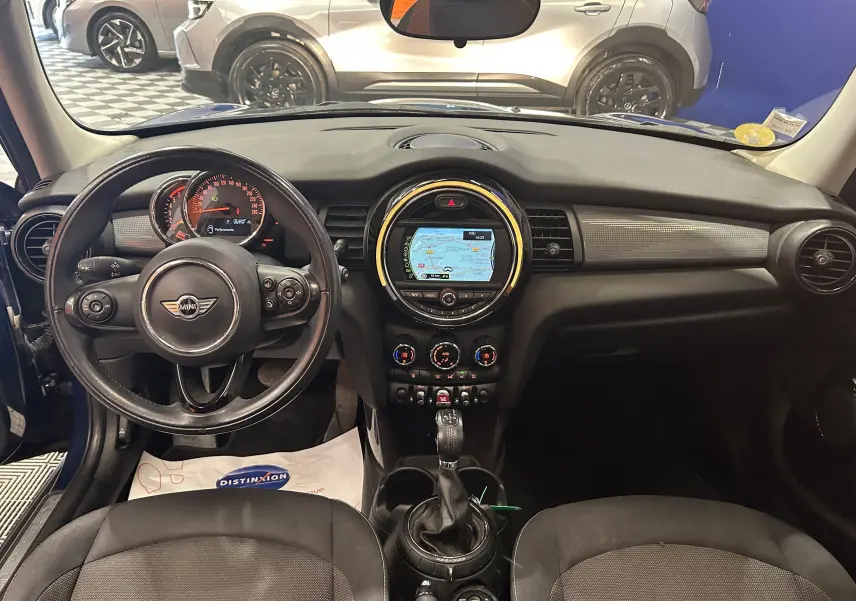 Vue intérieure du tableau de bord de la MINI 5P Cooper D bleu, avec volant cuir et écran GPS central allumé.