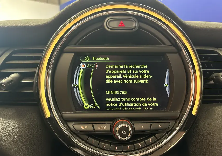 Gros plan sur l'écran central rond du tableau de bord d'une MINI 5P bleu, affichant le menu Bluetooth en jaune.