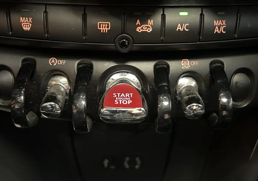Gros plan sur les commandes centrales du tableau de bord d'une MINI 5P, avec bouton rouge Start Engine Stop et interrupteurs noirs.