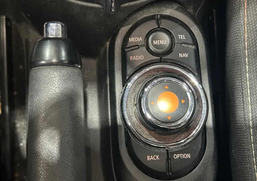 Gros plan sur la molette de commande centrale et frein à main en cuir noir dans une MINI 5 portes bleu de 2015.