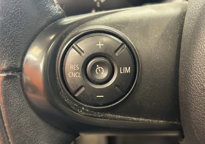 Gros plan sur les commandes de régulateur de vitesse au volant d'une MINI 5P Cooper D 2015, finition noire.