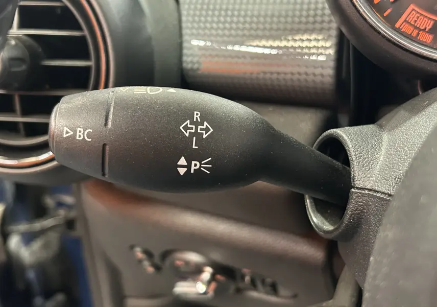 Gros plan sur la manette de clignotants noire du MINI 5P Cooper D 2015, avec tableau de bord carbone en arrière-plan.