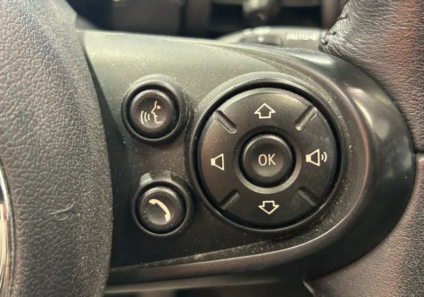 Gros plan sur les commandes multifonctions noires du volant côté gauche d’une MINI 5 portes bleu 2015.