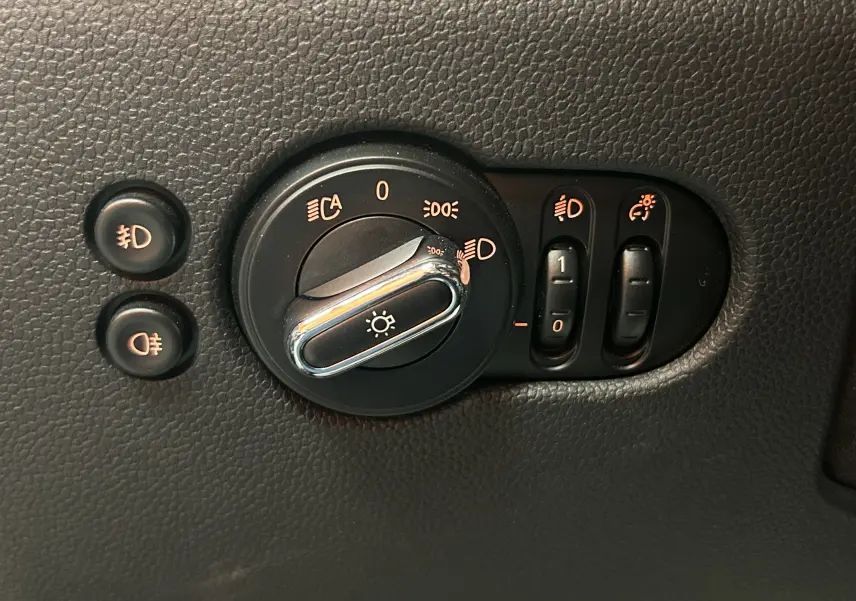 Gros plan sur la commande d’éclairage et réglages des phares du tableau de bord d’une MINI 5 portes bleu.