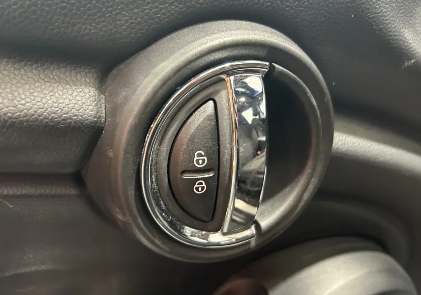 Gros plan sur la poignée intérieure de porte noire et chrome avec boutons de verrouillage dans une MINI 5P bleu de 2015.