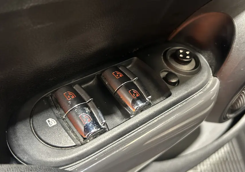 Gros plan sur les commandes des vitres électriques côté conducteur d’une MINI 5 portes bleu, avec réglage des rétroviseurs.