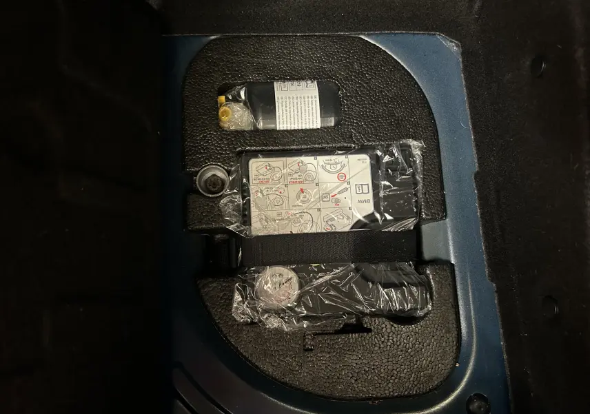 Vue rapprochée du coffre d’une MINI 5 portes bleu, montrant un kit de réparation pneu emballé dans son compartiment.