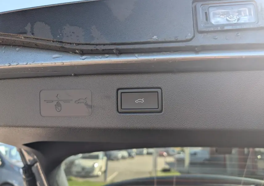Bouton d'ouverture électrique du coffre sur le hayon intérieur d'un Volkswagen T-Roc gris, vue rapprochée.