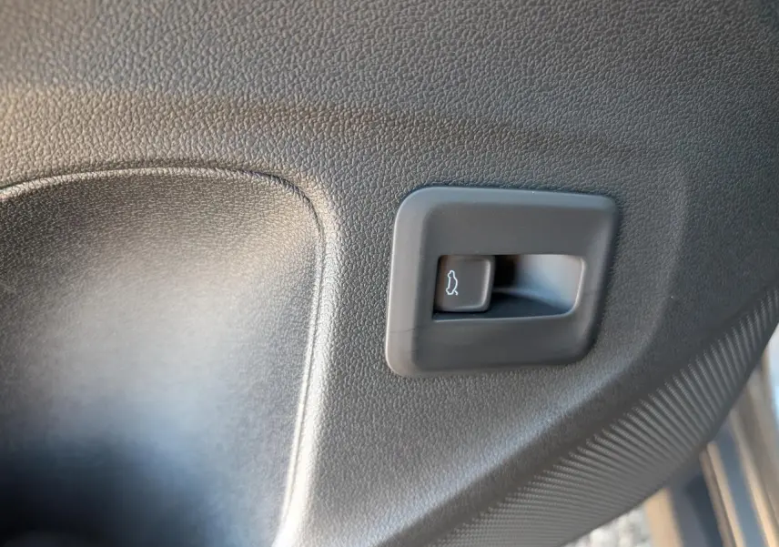 Gros plan sur le bouton d'ouverture électrique du coffre, intégré dans le panneau intérieur noir du Volkswagen T-Roc gris.