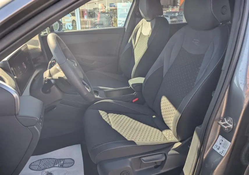Vue intérieure côté gauche du poste de conduite du Volkswagen T-Roc gris, avec sièges sport R-Line en tissu et volant multifonction cuir.
