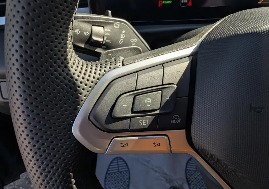 Gros plan sur le volant perforé gris et noir du Volkswagen T-Roc 2026, avec commandes intégrées et affichage digital en arrière-plan.