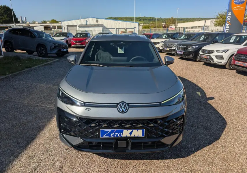 Volkswagen T-Roc gris métallisé en vue frontale, avec calandre noire et logo VW éclairé.