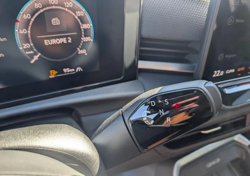Gros plan sur la commande de boîte automatique DSG 7 du Volkswagen T-Roc gris, avec tableau de bord digital en arrière-plan.