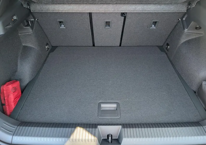 Vue plongeante sur le coffre gris du Volkswagen T-Roc 1.5 eTSI Hybrid Evo2 avec tapis plat et trousse de secours rouge.