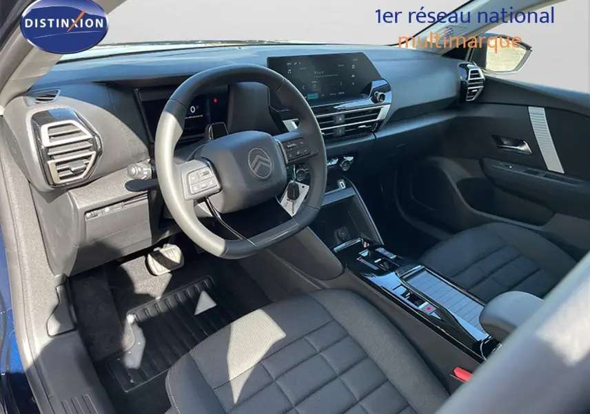 Vue intérieure côté conducteur de la Citroën C4 Hybrid 2026, avec tableau de bord moderne et sièges tissu gris.