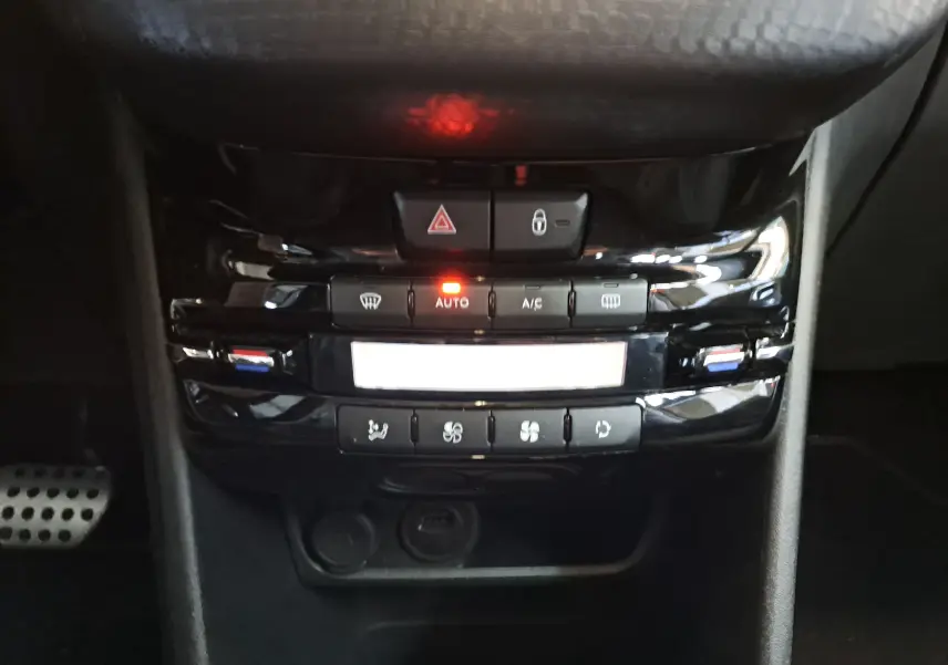 Panneau de commande de climatisation automatique noir brillant avec boutons éclairés rouge et symboles blancs dans un Peugeot 2008 gris de 2019.