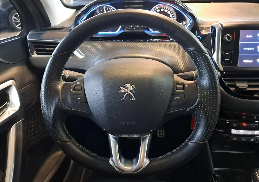 Volant en cuir noir avec logo Peugeot au centre, tableau de bord éclairé en bleu et écran tactile à droite.