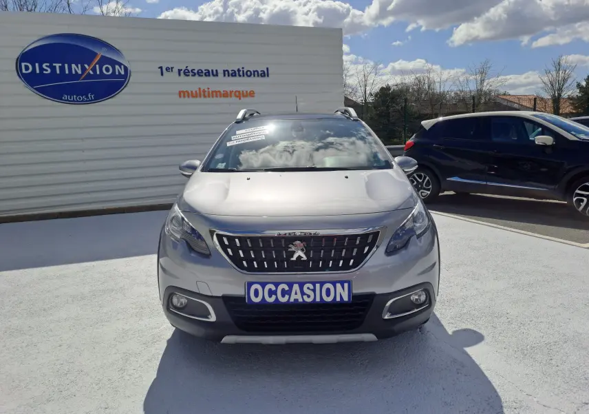 Peugeot 2008 gris vue de face, avec plaque "OCCASION" et toit équipé de barres de toit sur parking extérieur.