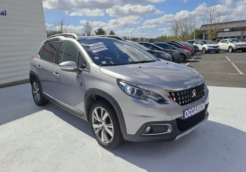 Peugeot 2008 gris en 3/4 avant droit, avec calandre chromée et jantes alliage, stationné en extérieur sous ciel bleu.