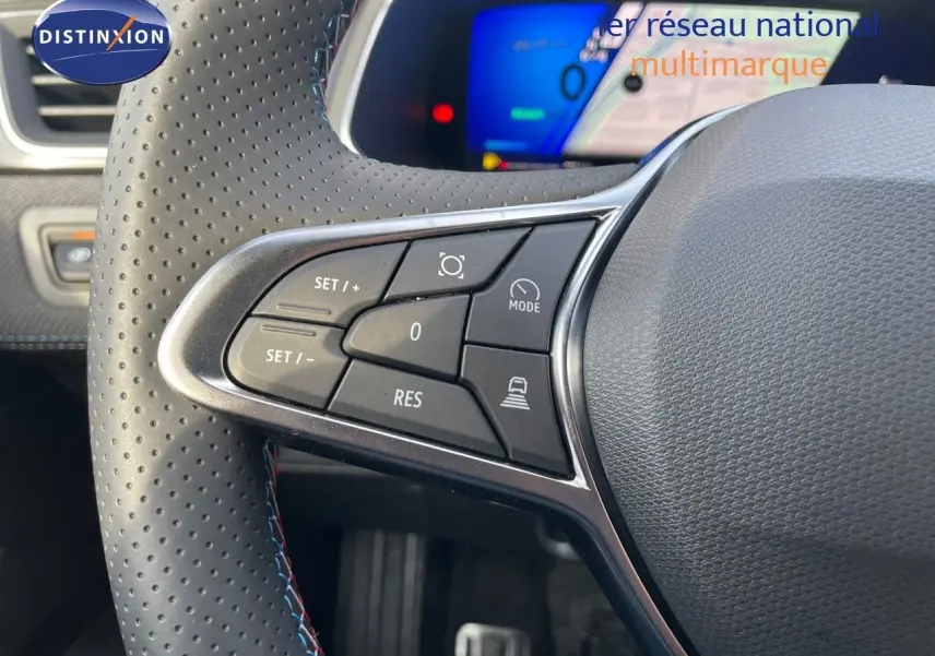 Gros plan sur le volant perforé avec commandes intégrées du Renault Symbioz gris Rafale, tableau de bord numérique en arrière-plan.