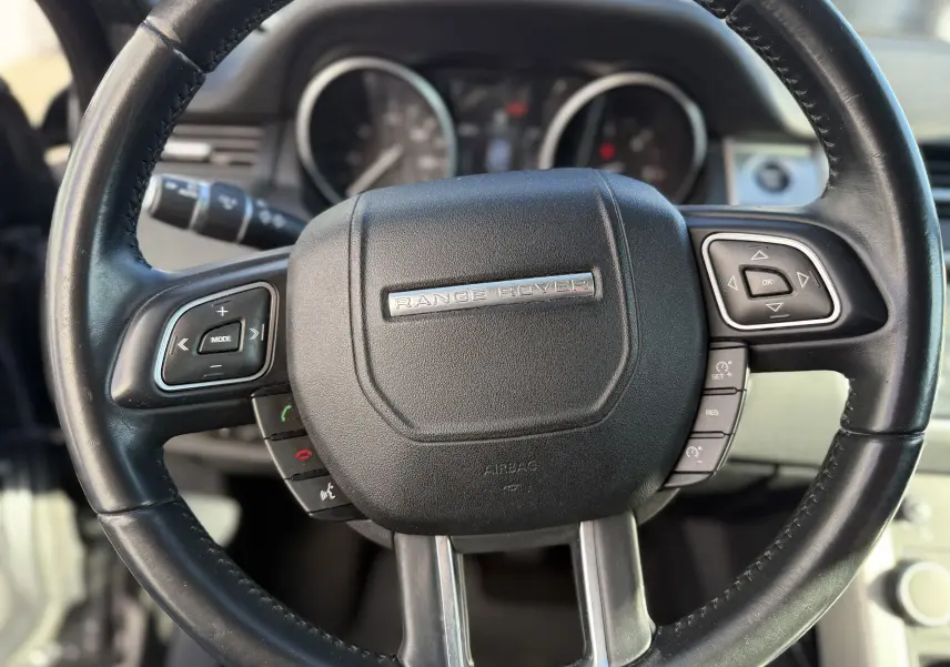 Gros plan sur le volant noir du Range Rover Evoque gris, avec commandes intégrées et logo central argenté.