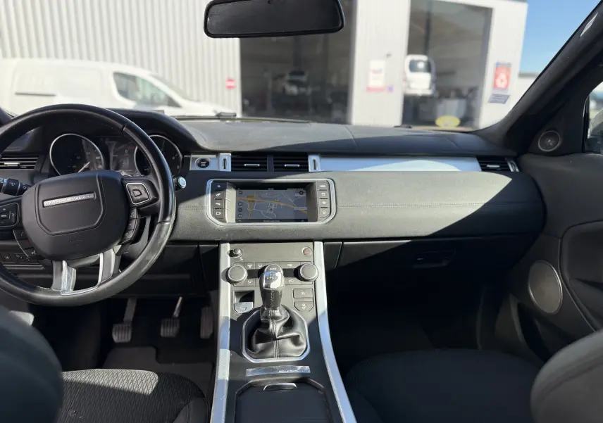Vue intérieure avant du Range Rover Evoque gris, montrant le tableau de bord avec écran tactile et volant multifonction.
