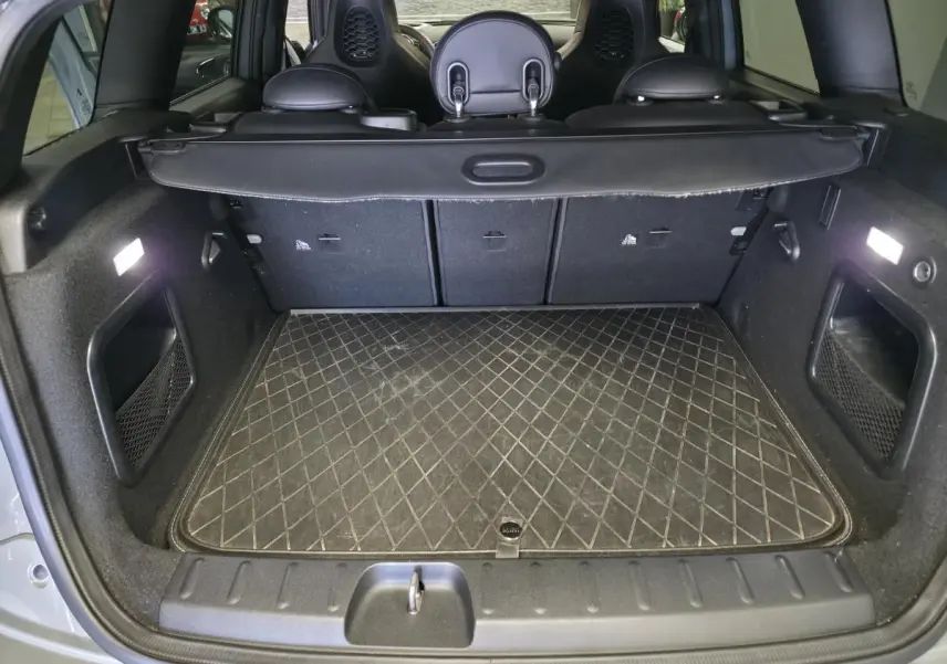 Coffre ouvert vu de l'arrière d'une MINI Clubman gris Moonwalk avec tapis de sol matelassé et banquette rabattable.