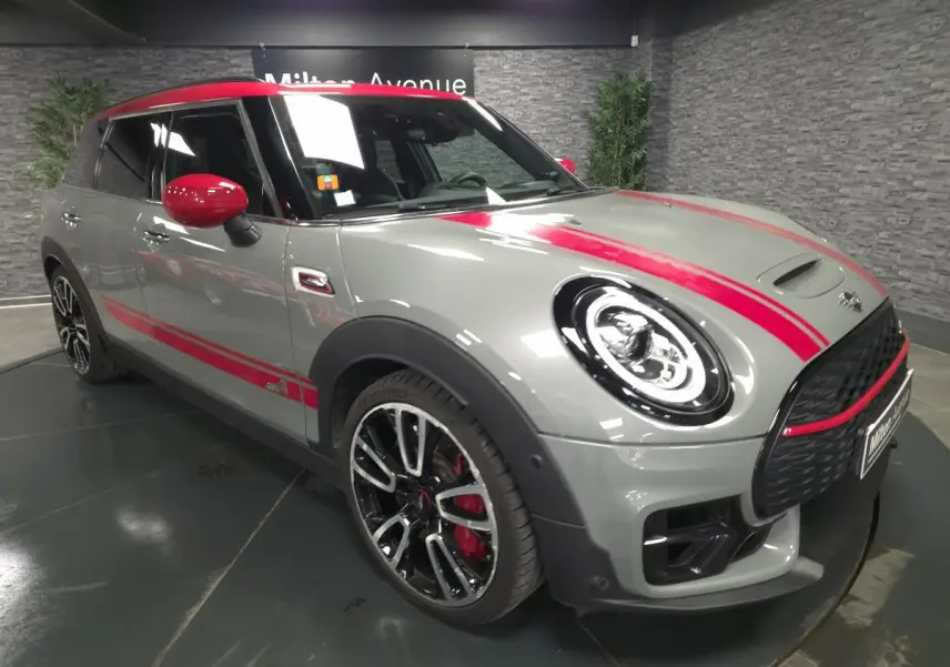 MINI Clubman John Cooper Works gris avec bandes rouges, vue 3/4 avant mettant en valeur jantes et toit rouge.