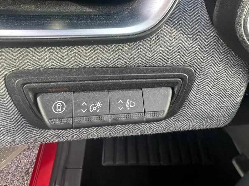 Gros plan sur les commandes d’éclairage et verrouillage, entourées d’un tissu gris à motif chevrons, intérieur Renault Clio Rouge Flamme 2025.