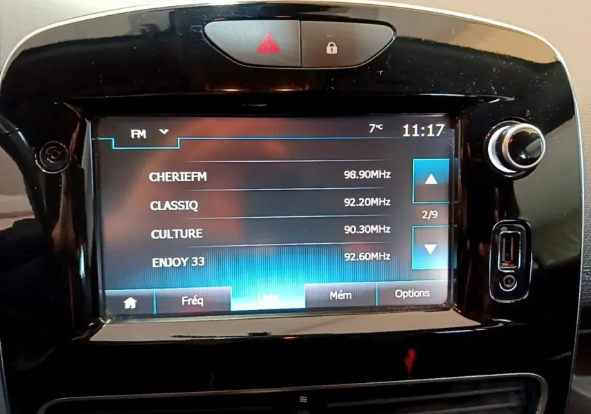 Écran tactile central de la Renault Clio Zen Energy 2016 affichant les stations radio FM, entouré de boutons noirs brillants.