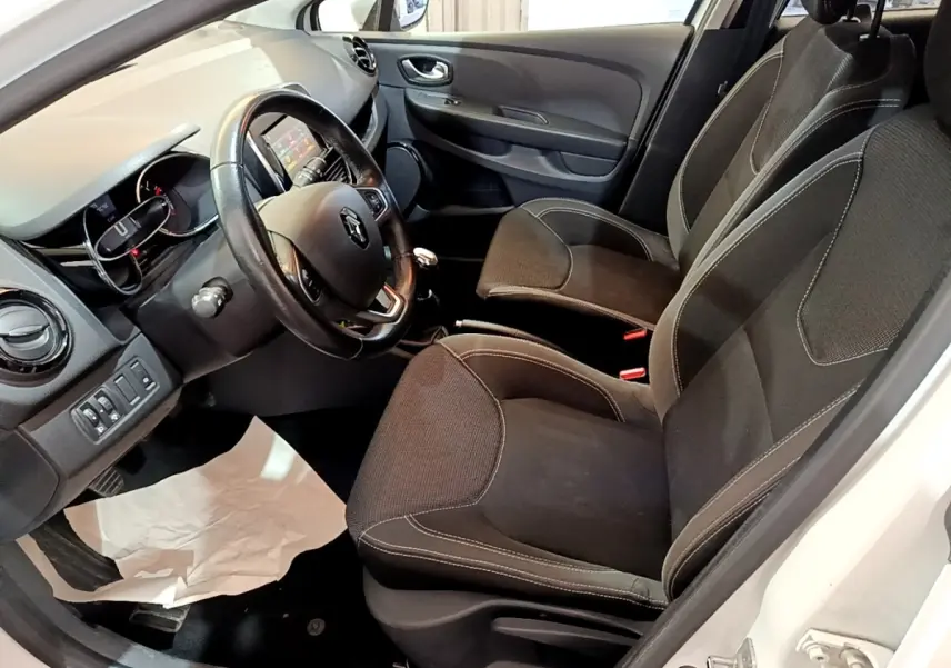 Vue intérieure côté conducteur de la Renault Clio Zen Energy dCi 75 blanche, volant cuir et sièges noirs avec coutures contrastées.