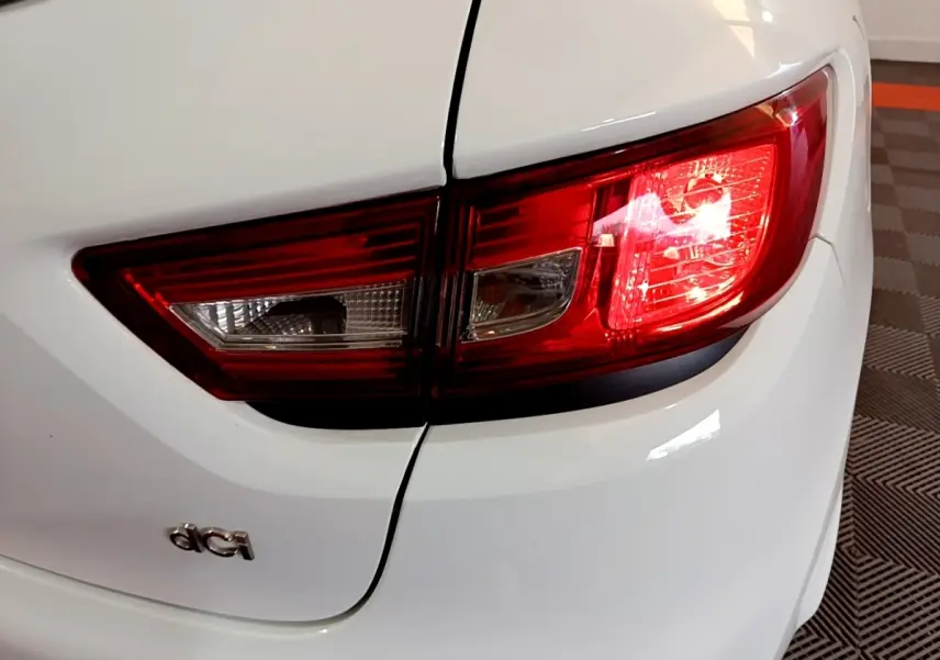 Gros plan sur le feu arrière droit rouge et blanc d'une Renault Clio blanche avec logo dCi visible sur le coffre.