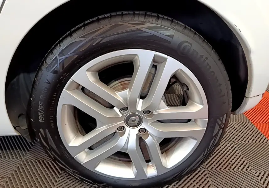 Gros plan sur la roue avant droite d'une Renault Clio blanche, jante alliage à cinq branches doubles.