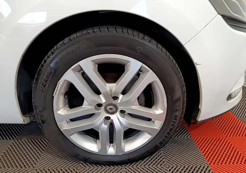 Gros plan sur la roue avant gauche d'une Renault Clio blanche, jante alliage argent avec logo Renault au centre.