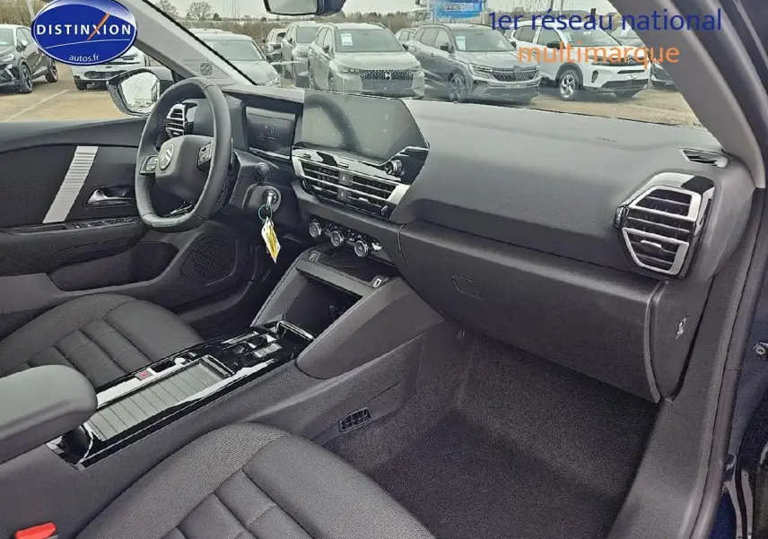 Intérieur avant droit de la Citroën C4 1.2 hybride 136 plus bleu eclipse avec tableau de bord moderne et sièges tissu noir.