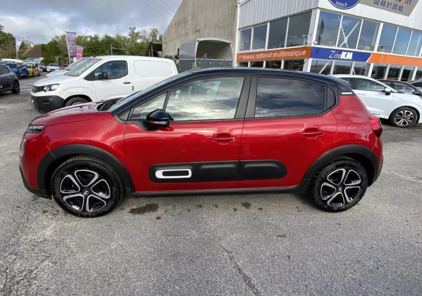 Profil latéral gauche d'une Citroën C3 rouge Elixir avec toit noir et protections latérales noires distinctives.
