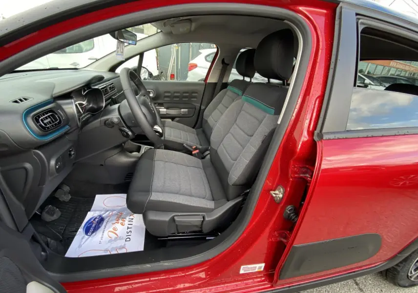 Vue intérieure côté conducteur d'une Citroën C3 2021 rouge Elixir avec sièges gris et tableau de bord noir.