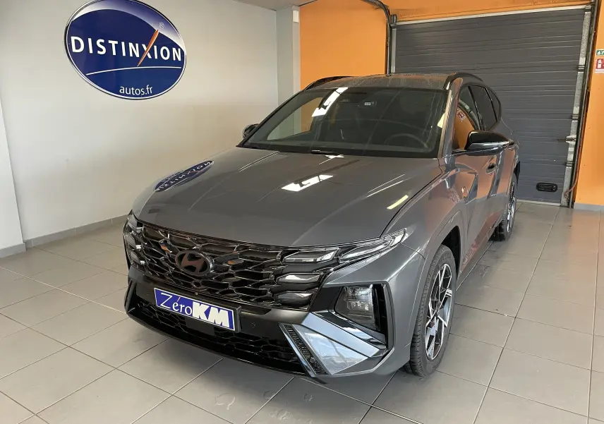 Vue 3/4 avant d'un Hyundai Tucson gris Ecotronic avec calandre noire et jantes alliage en intérieur showroom.