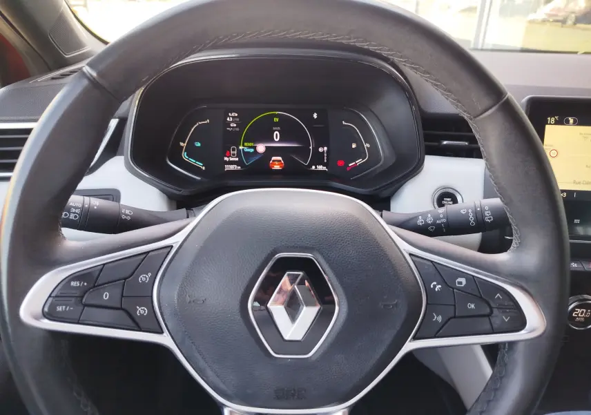 Vue rapprochée du volant noir avec logo Renault et tableau de bord numérique de la Clio hybride orange Valencia 2022.