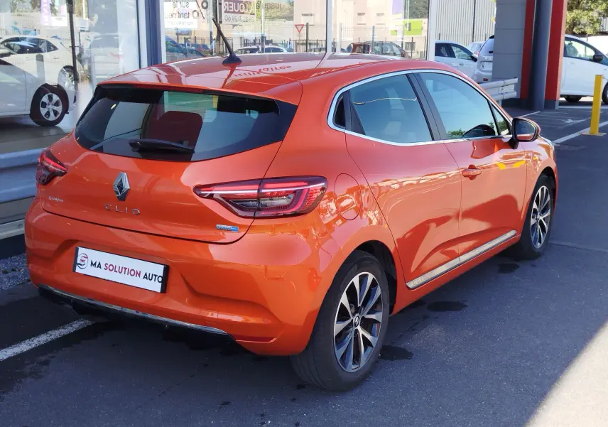 Vue 3/4 arrière droite d'une Renault Clio 1.6 E-Tech hybride 140ch Intens 2022 en Orange Valencia, avec jantes alliage et feux LED.