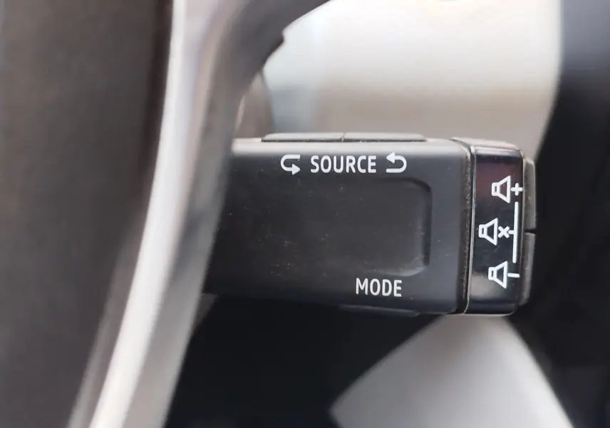 Gros plan sur la commande au volant gauche de la Renault Clio 1.6 E-Tech hybride orange, avec boutons source et mode.