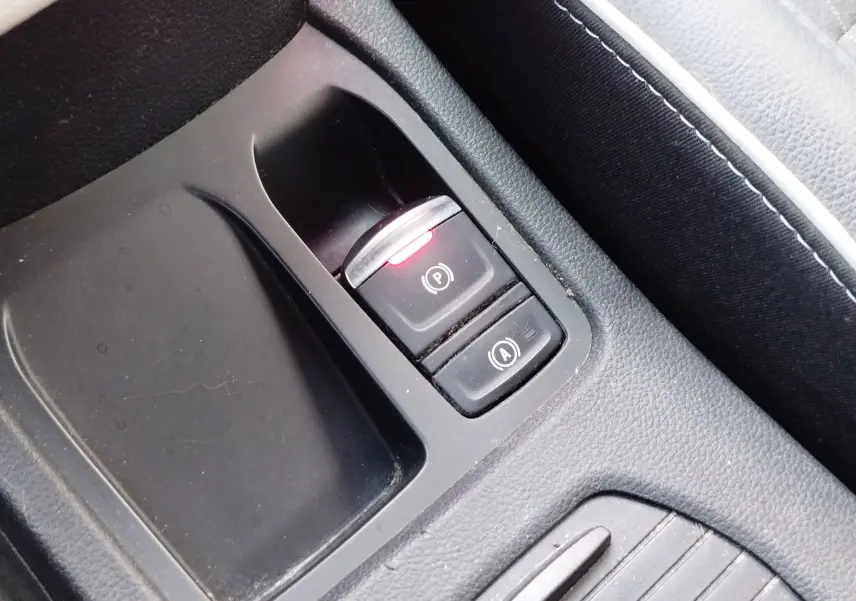 Gros plan sur la console centrale noire de la Renault Clio 1.6 E-Tech avec bouton de frein à main électronique allumé.